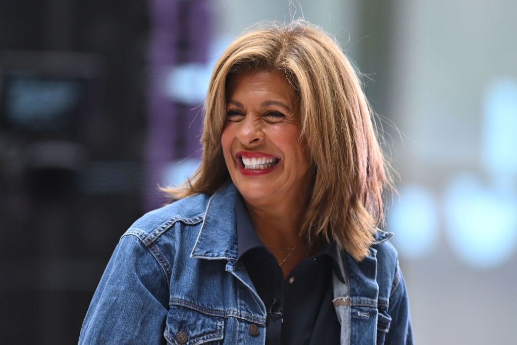 Hoda Kotb is smiling broadly, wearing a denim jacket over a dark top