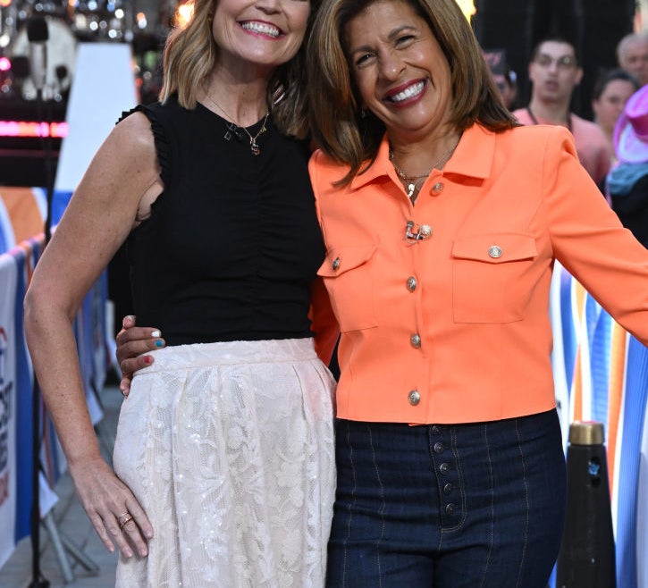 Savannah Guthrie in a black sleeveless top and lace skirt, with Hoda Kotb in an orange jacket and jeans, smiling and posing together at an outdoor event