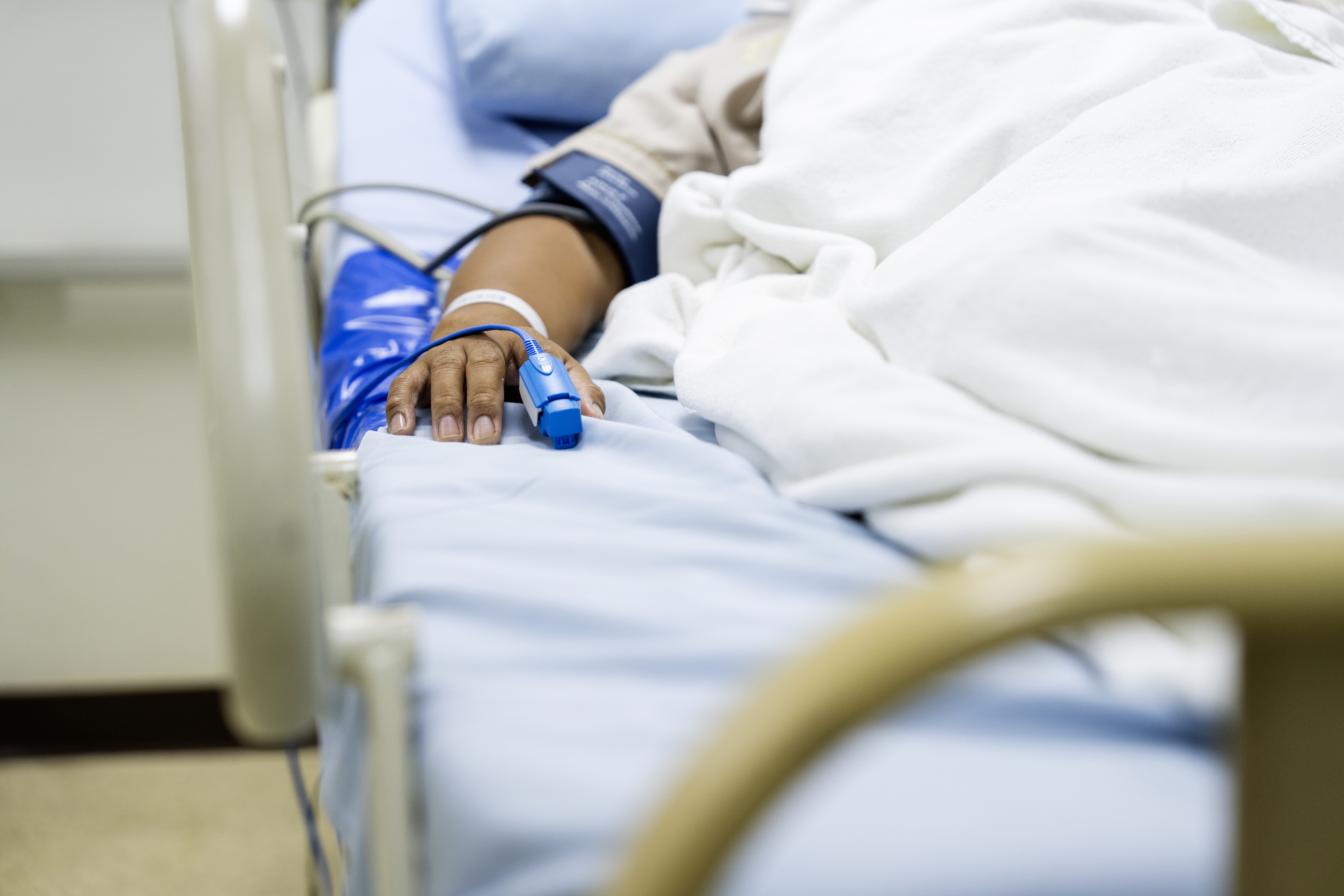 Person lying in a hospital bed with a blood pressure cuff on their arm and a pulse oximeter on their finger