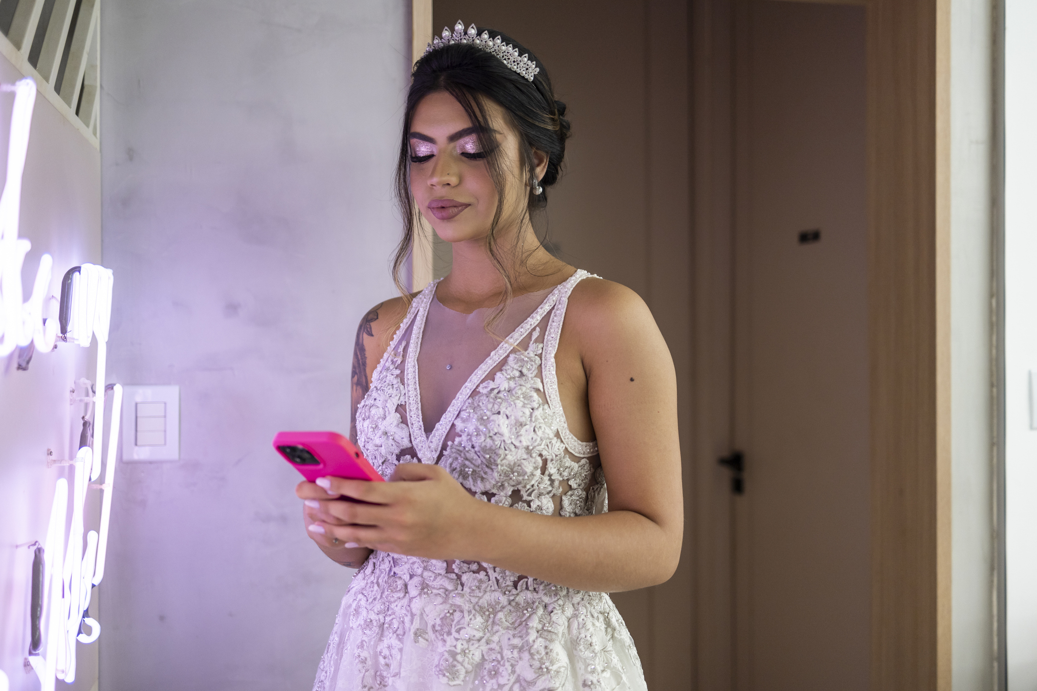 Bride in a lace wedding gown and tiara using a pink phone