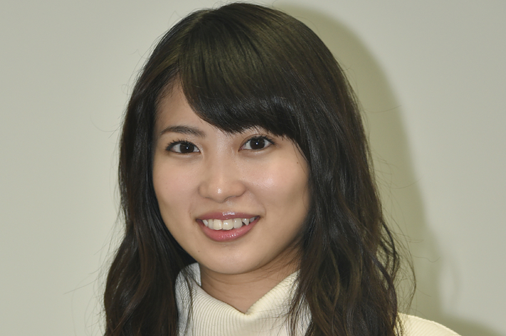 女性が微笑んでカメラを見ています。白のタートルネックのセーターを着ています。