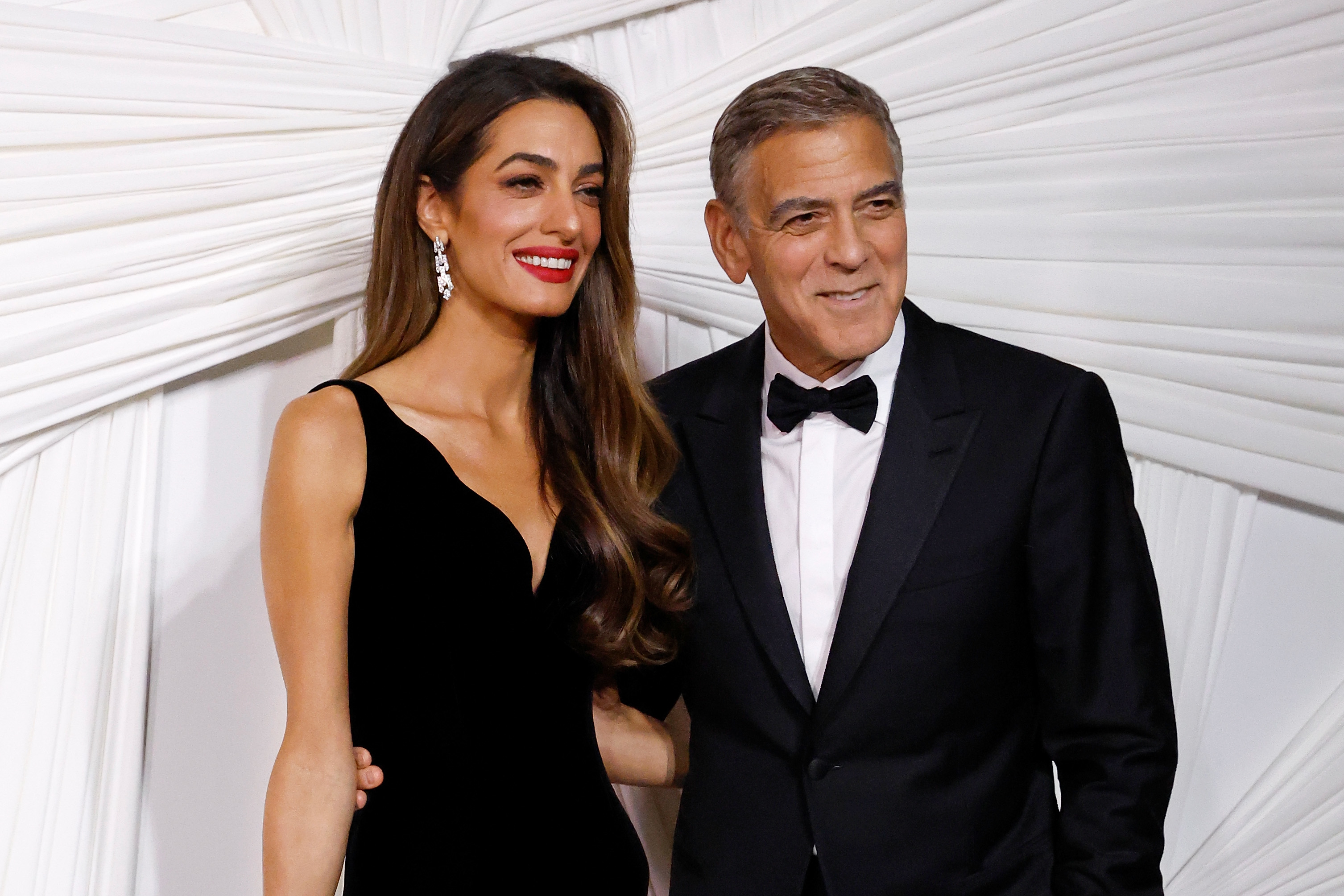 Amal Clooney in a sleek dark gown and George Clooney in a dark tuxedo pose together at an event