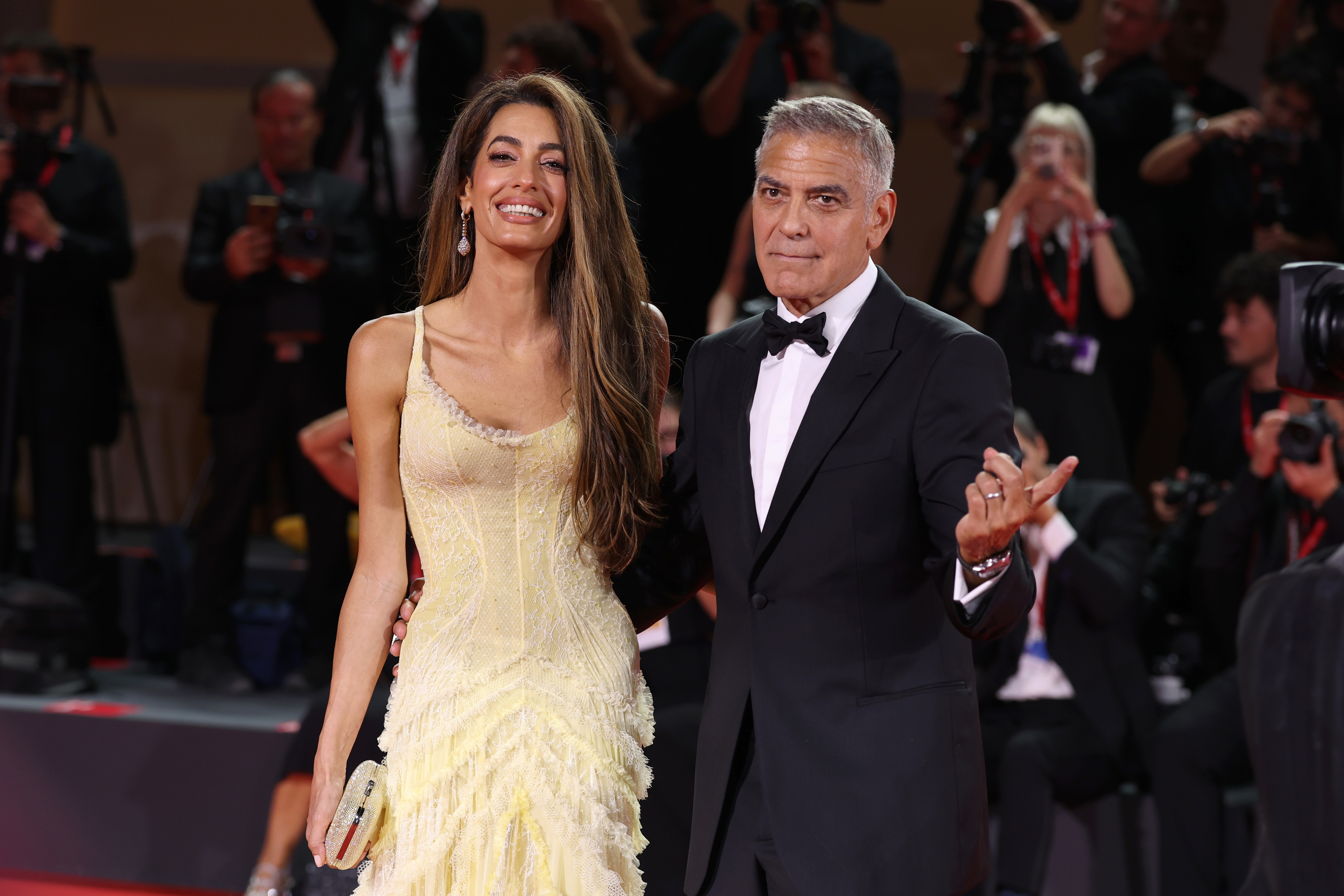 Amal Clooney in a chic, strapless gown and George Clooney in a tuxedo walk the red carpet as photographers capture the moment