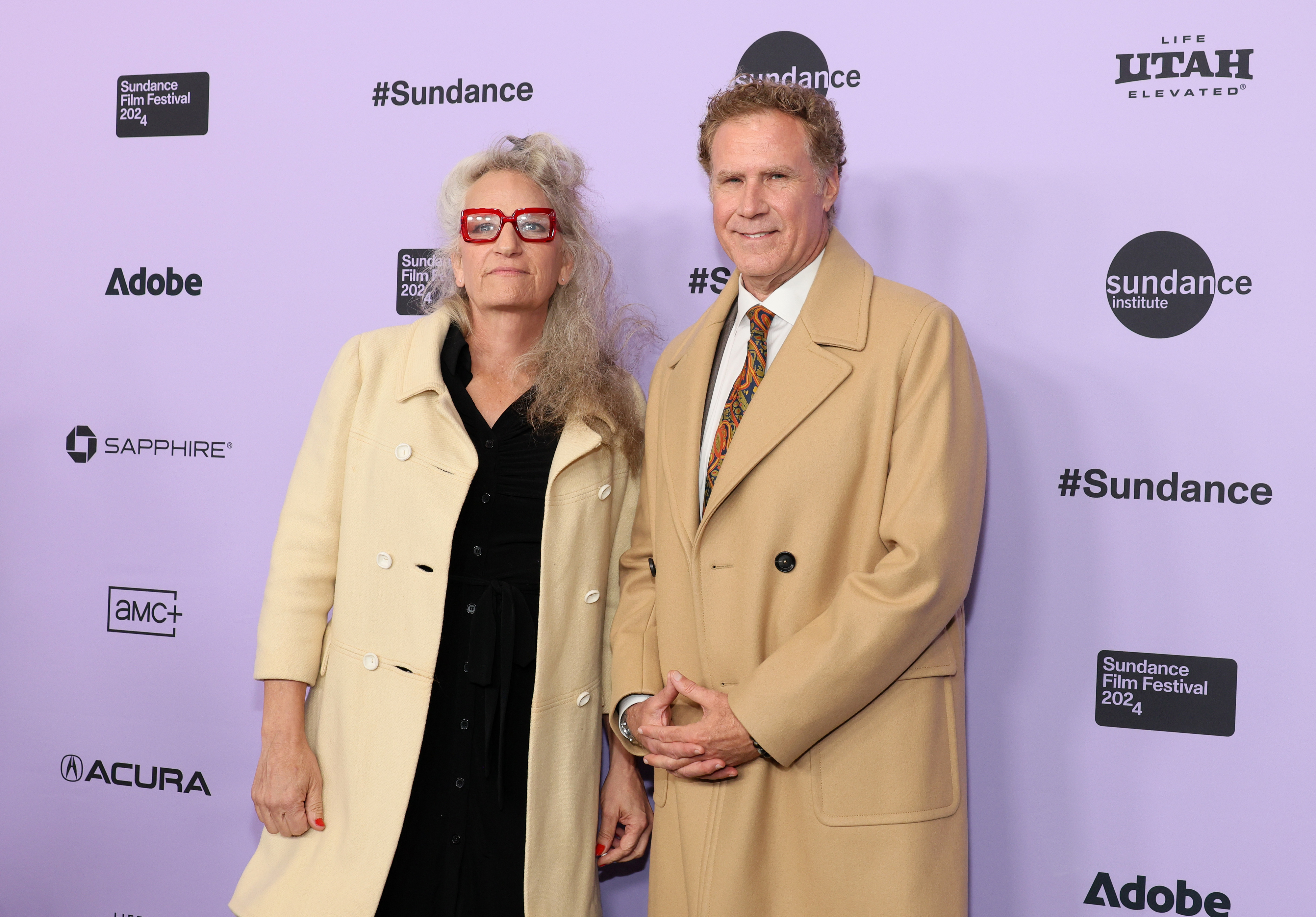 Harper Steele and Will Ferrell attend the Sundance Film Festival, both wearing long beige coats, standing in front of a backdrop with festival and sponsor logos