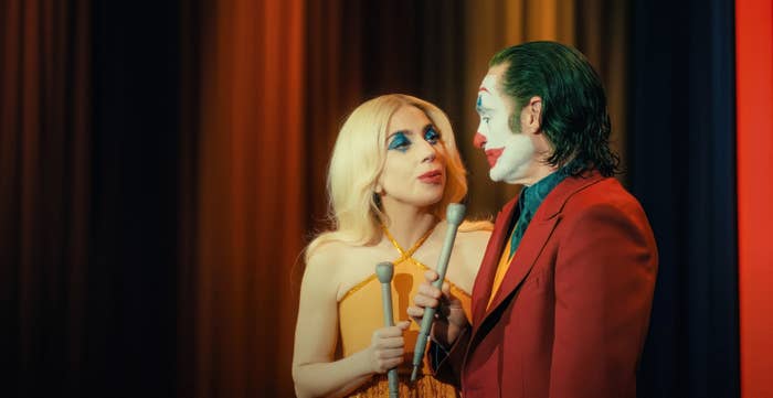 Lady Gaga in a halter dress and Joaquin Phoenix dressed as the Joker, both holding microphones, on a stage