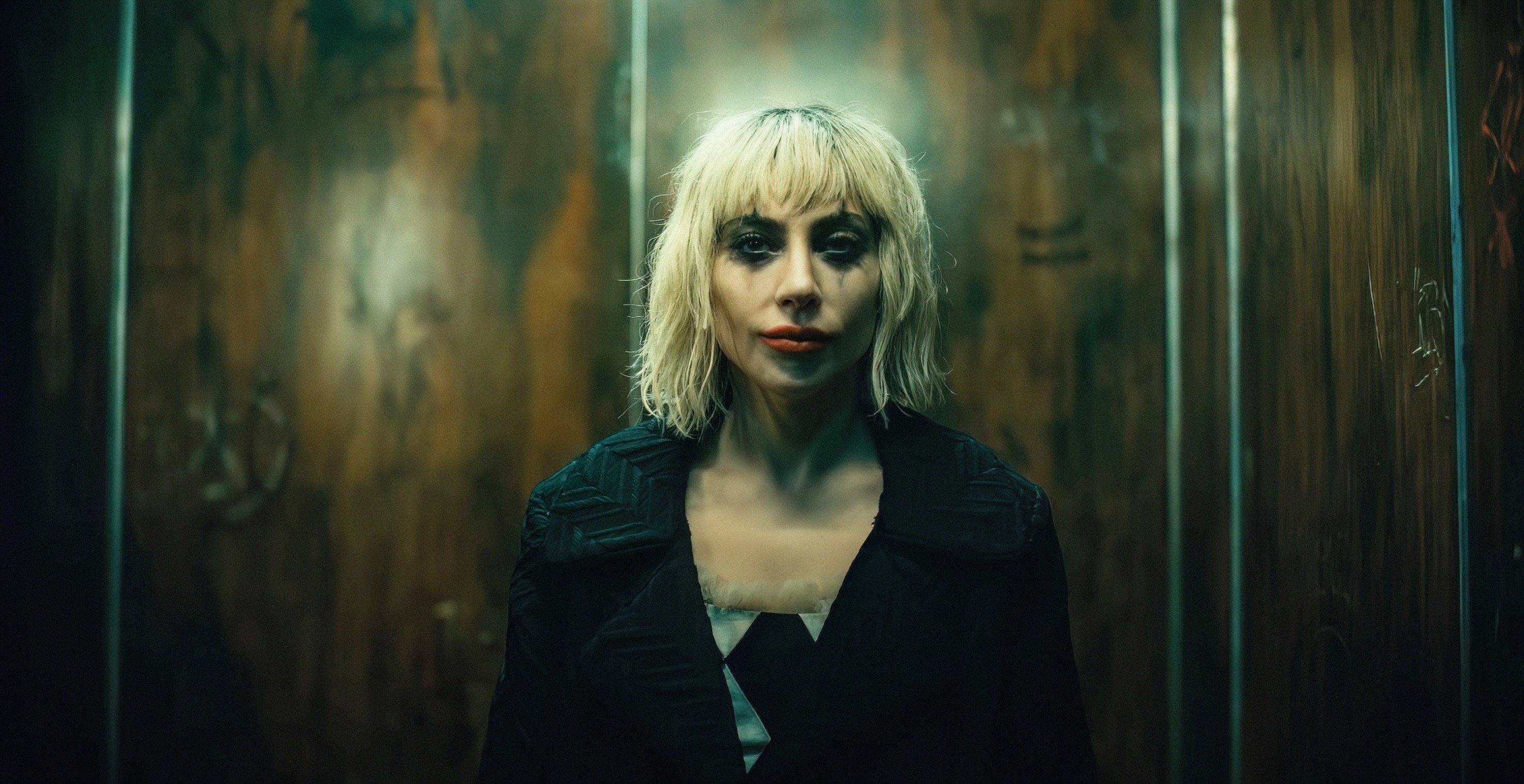Lady Gaga in an elevator, wearing a stylish dark jacket with a top, and a striking blunt bob haircut
