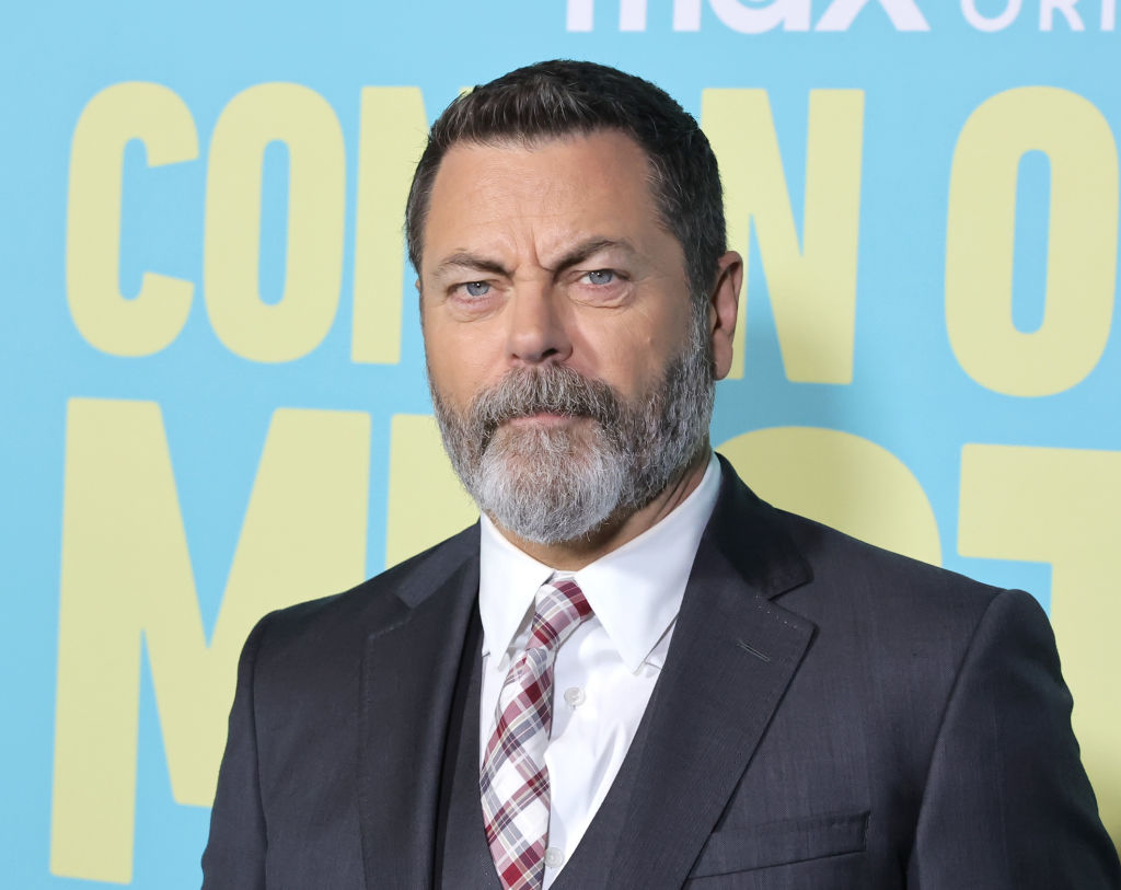 Nick Offerman on the red carpet, wearing a dark suit with a white shirt and plaid tie, at the premiere of an HBO Max original series