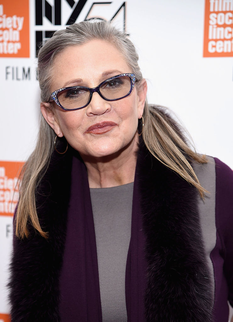 Carrie Fisher wearing sophisticated glasses and a fur-trimmed coat at a film event