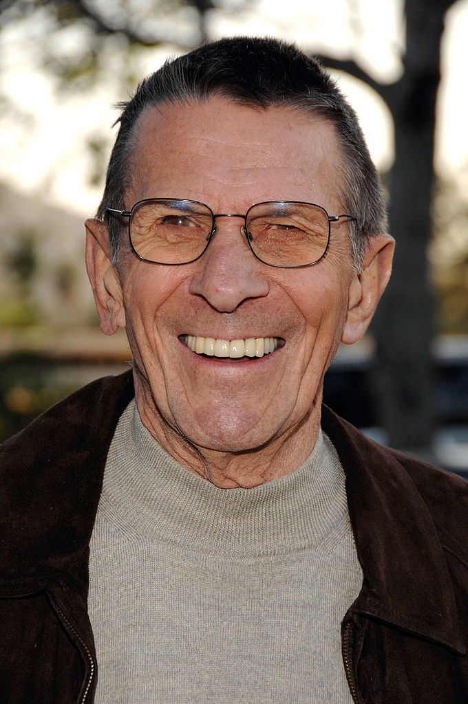 Leonard Nimoy smiles at an outdoor event, wearing glasses, a light turtleneck sweater, and a dark jacket