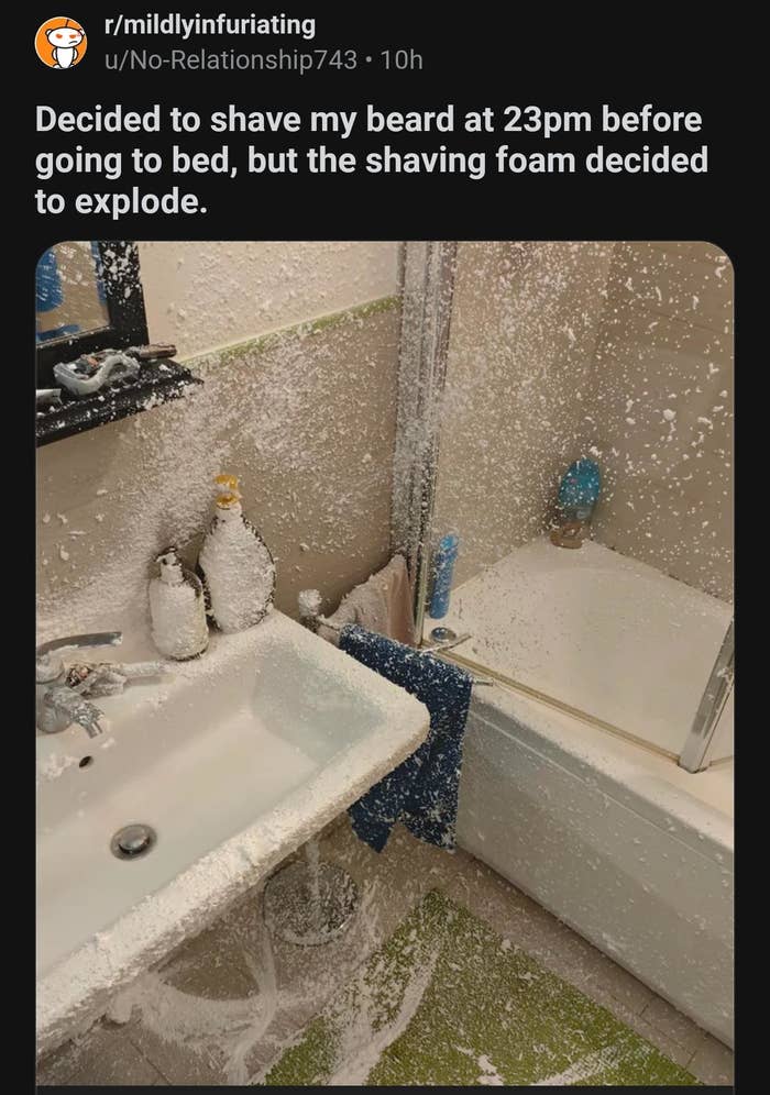 Bathroom covered in white shaving foam and debris, including sink and bathtub. Text: "Decided to shave my beard at 23pm before going to bed, but the shaving foam decided to explode."