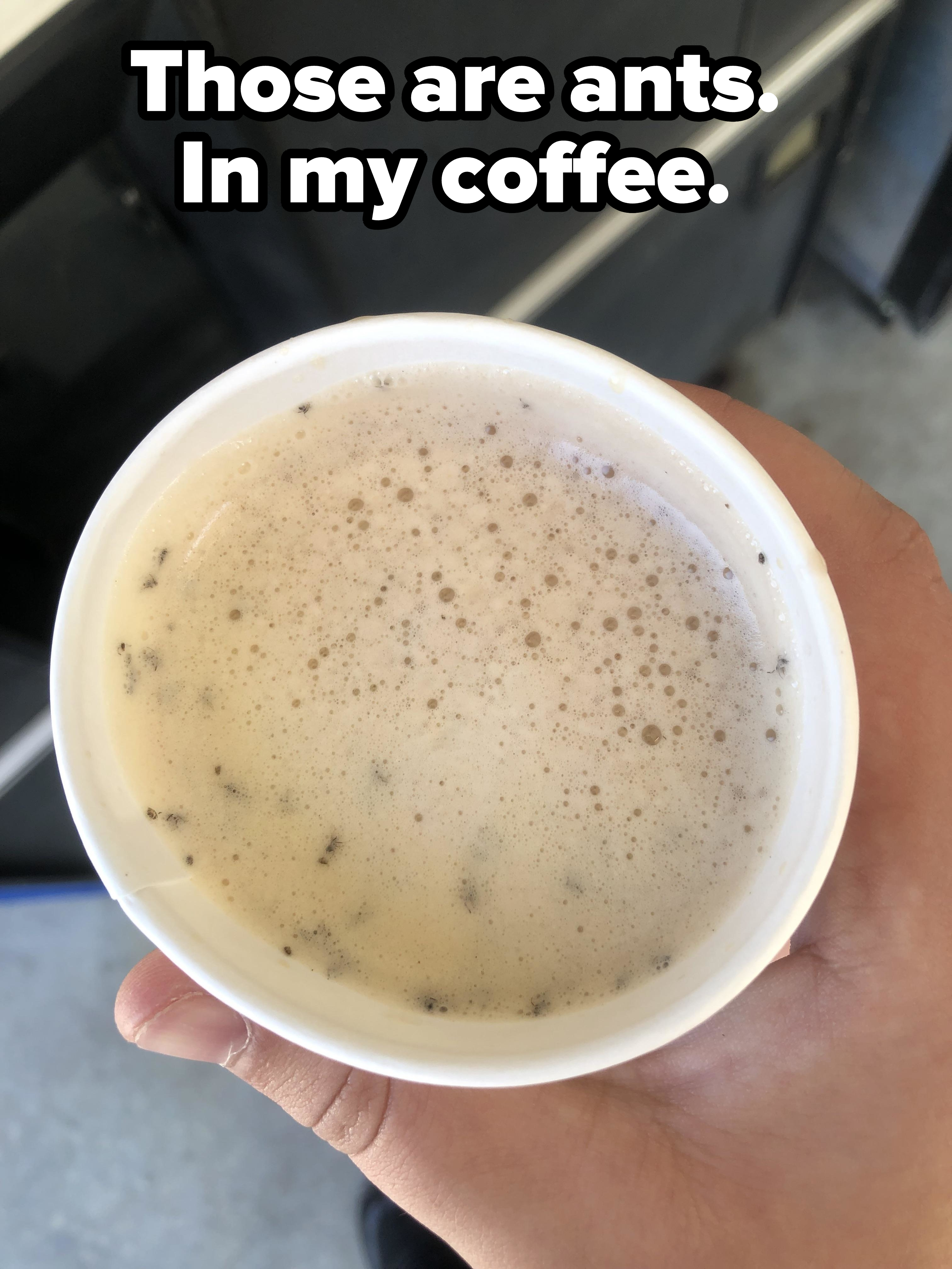 Hand holding a cup filled with a drink that has foam and small particles floating on the surface
