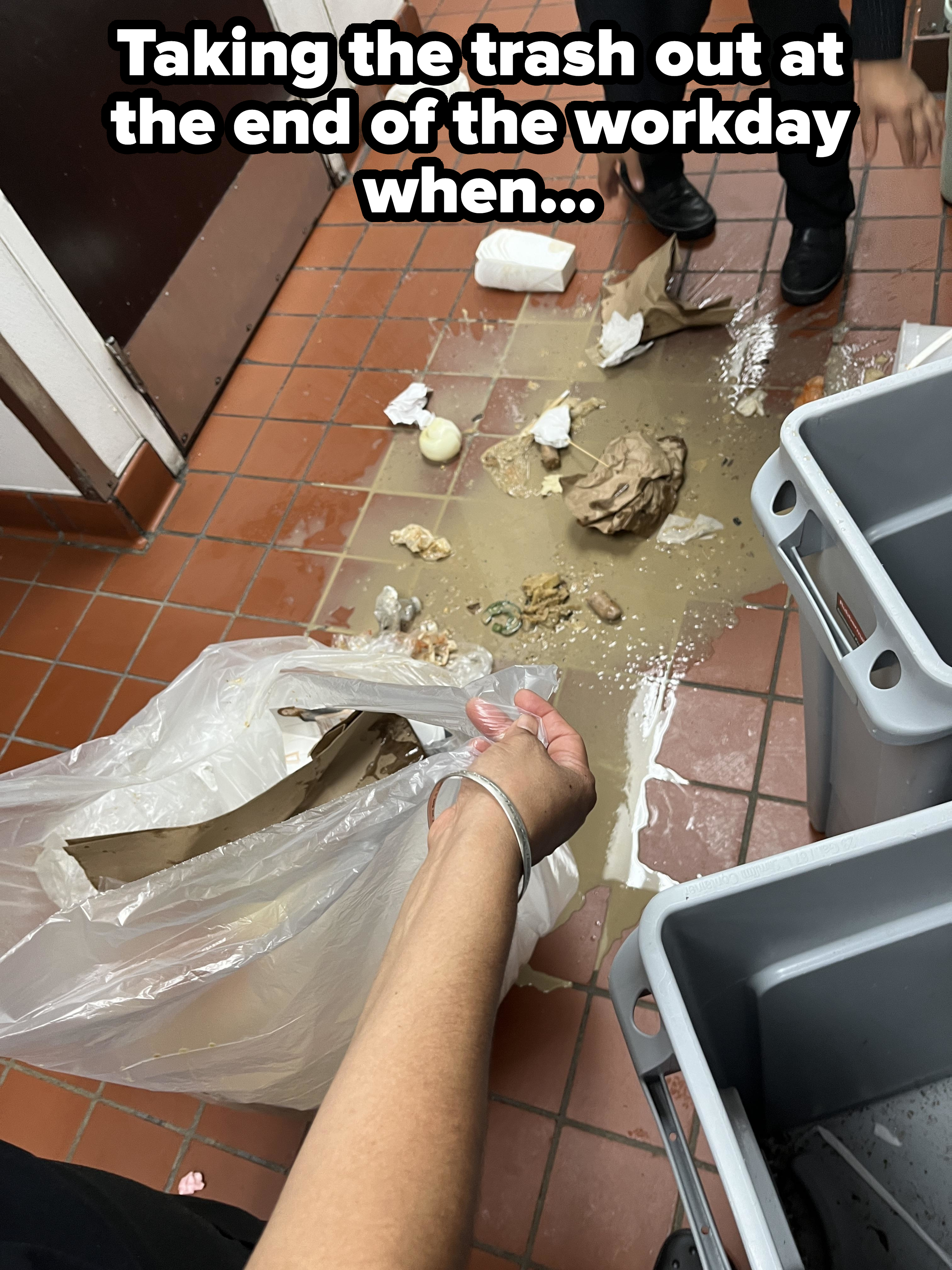A person is cleaning up a dropped bag of trash on a tiled floor. The mess includes crumpled paper, spilled liquid, and food scraps