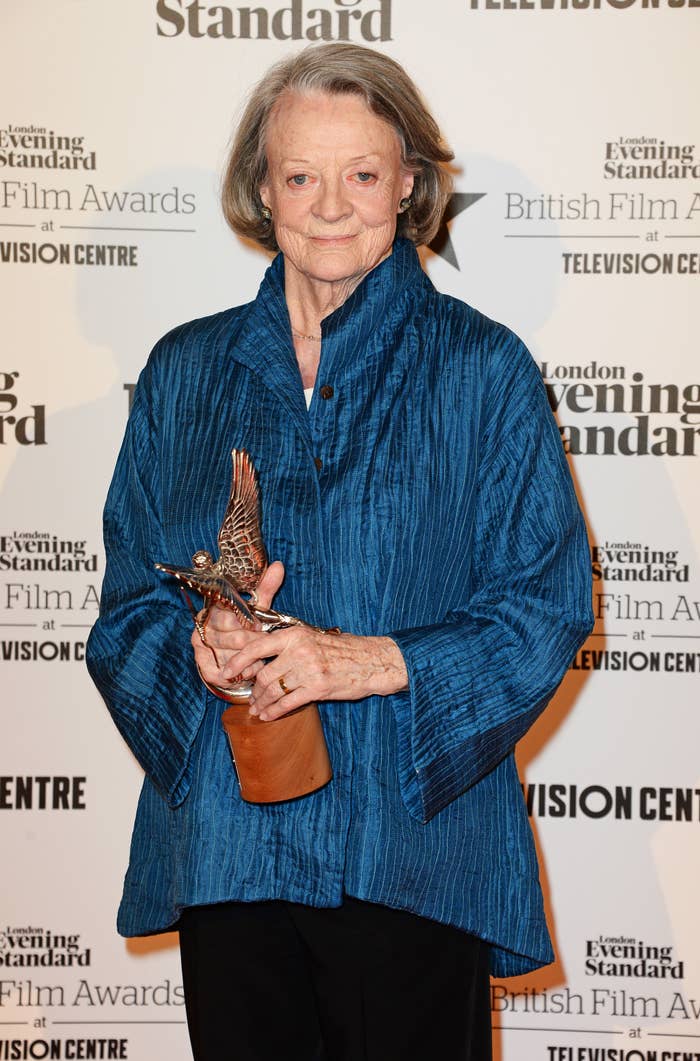 Maggie Smith holds an award while posing on the red carpet at the London Evening Standard British Film Awards. She is wearing a loose-fitting, textured jacket