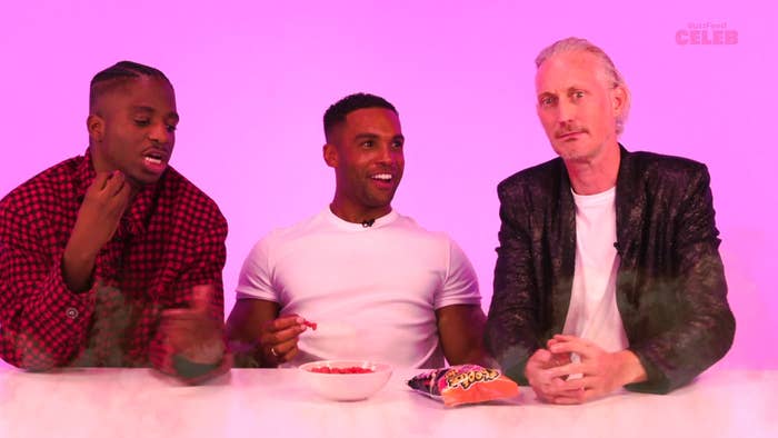 (L-R) Men in casual outfits sit at a table with a bowl of snacks