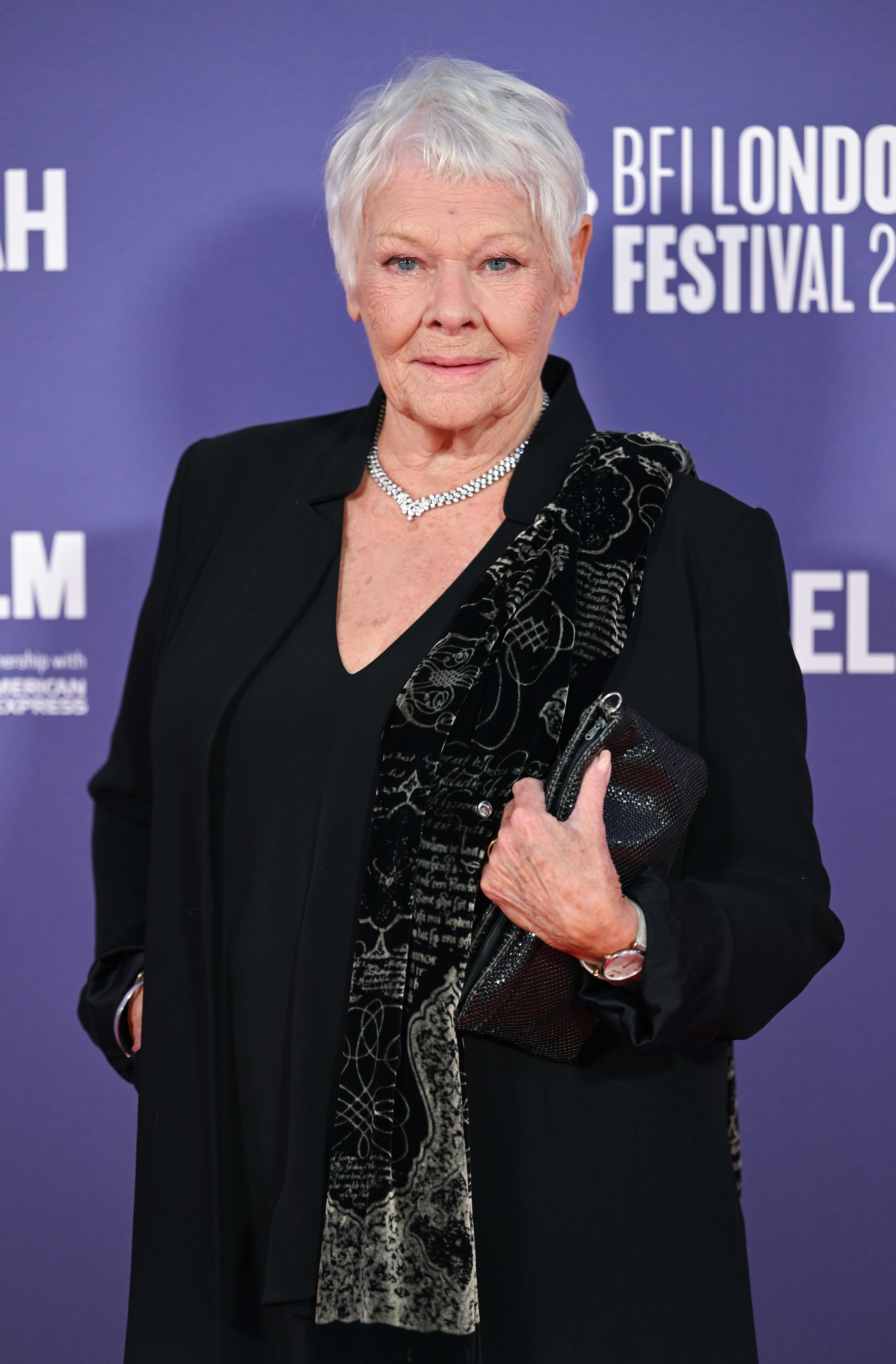 Judi Dench at the BFI London Film Festival 2022, wearing a black outfit with an elegant patterned shawl and holding a clutch