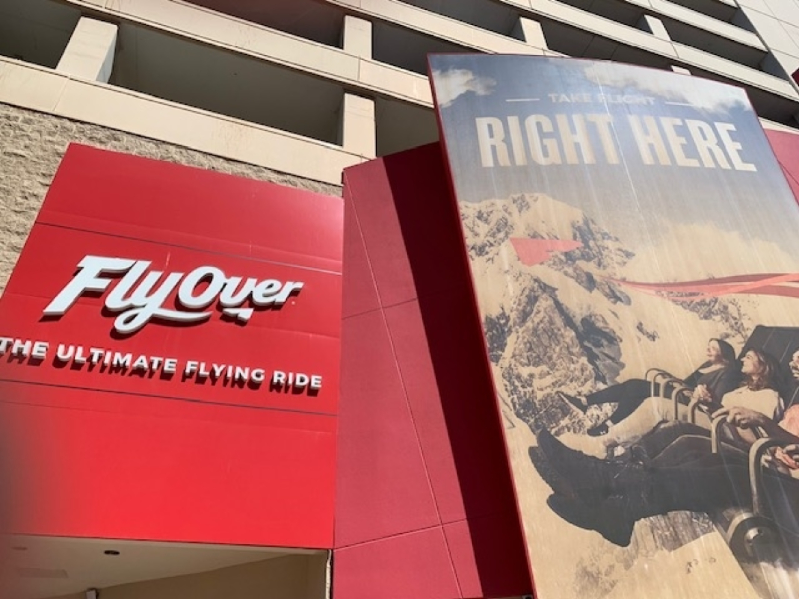 Entrance to FlyOver, an attraction offering a flight simulation experience, next to a large promotional banner with people enjoying a scenic aerial ride