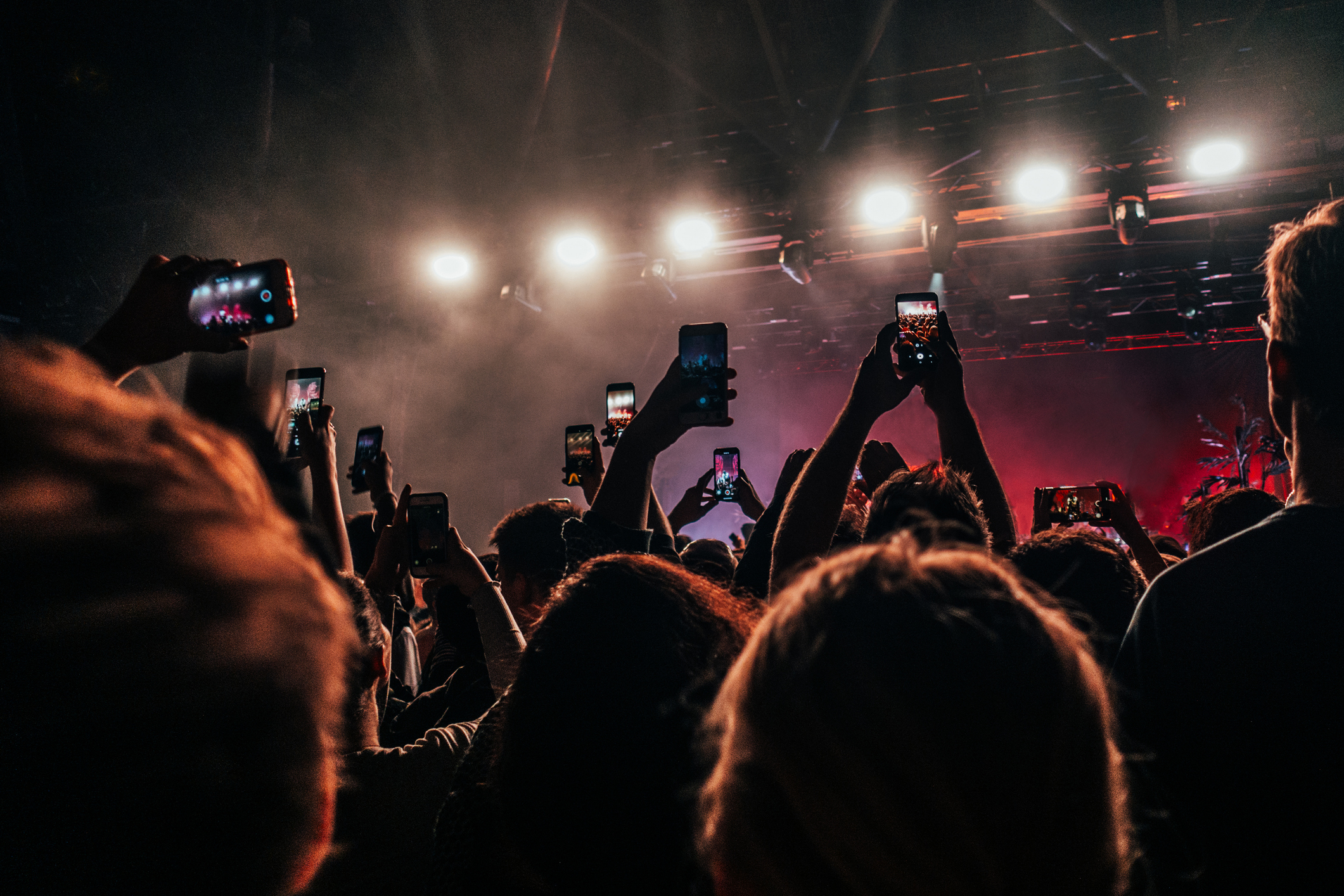 Crowd at a concert holding up phones to capture the performance, with bright stage lights illuminating the scene