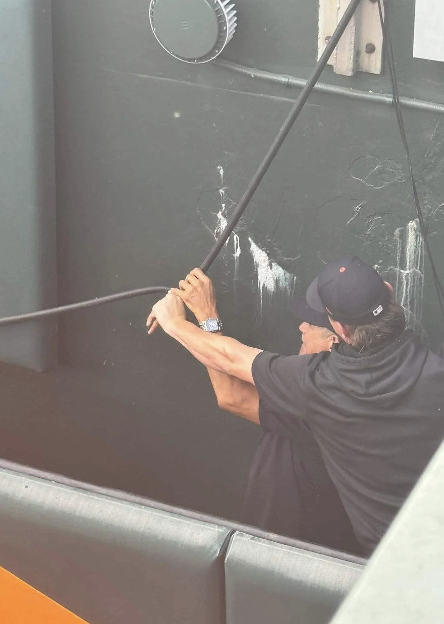 Two men, whose identities are unknown, work together using a long tool in what appears to be a maintenance or repair task