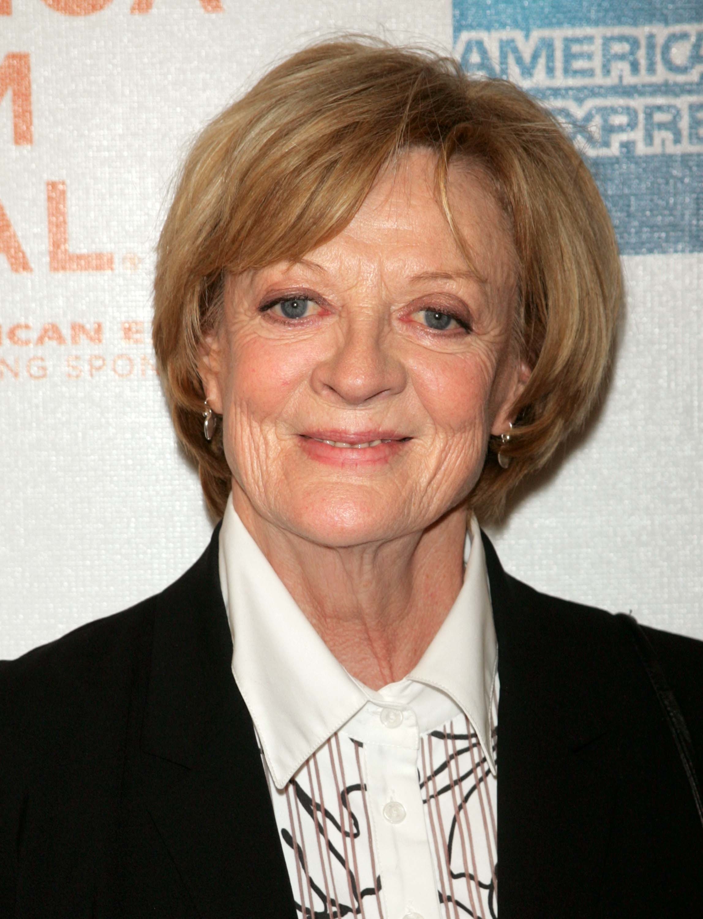 Maggie Smith at an event, wearing a blouse with a dark blazer and smiling at the camera