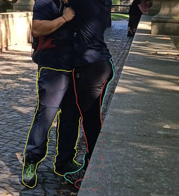 Two people outdoors in athletic wear, one tying the other's shoe, their arms around each other for support