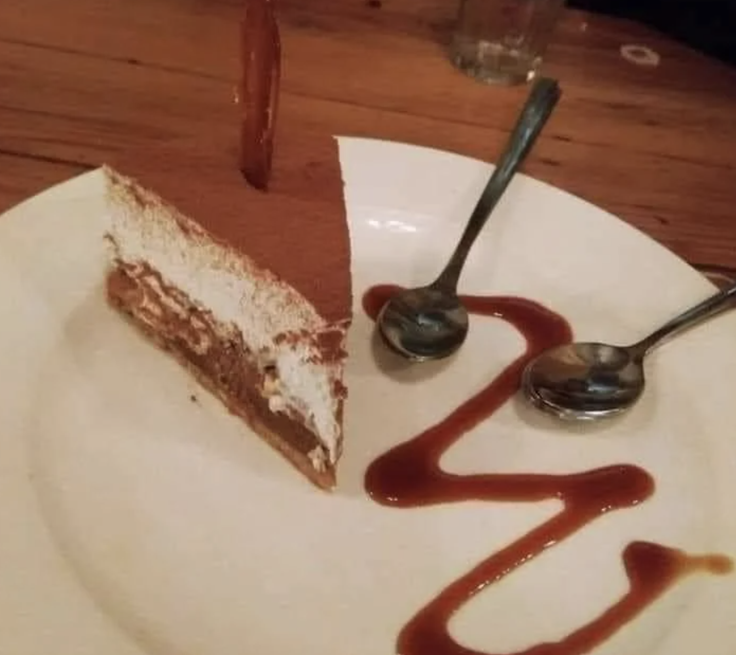 A slice of tiramisu on a plate with two spoons and caramel drizzle on the side