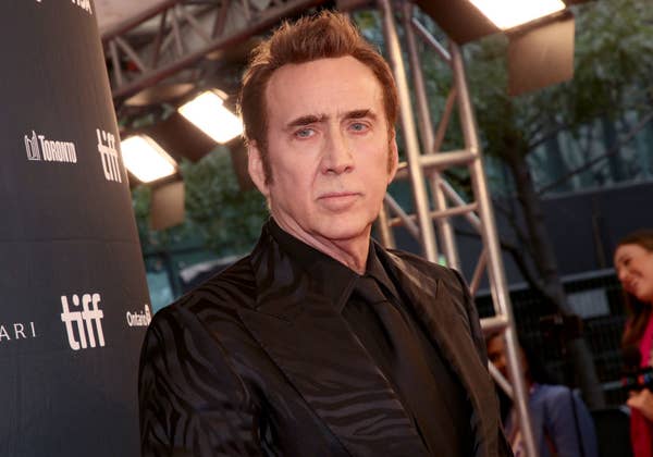 Nicolas Cage on the red carpet at the Toronto International Film Festival (TIFF), wearing a black patterned suit and black shirt