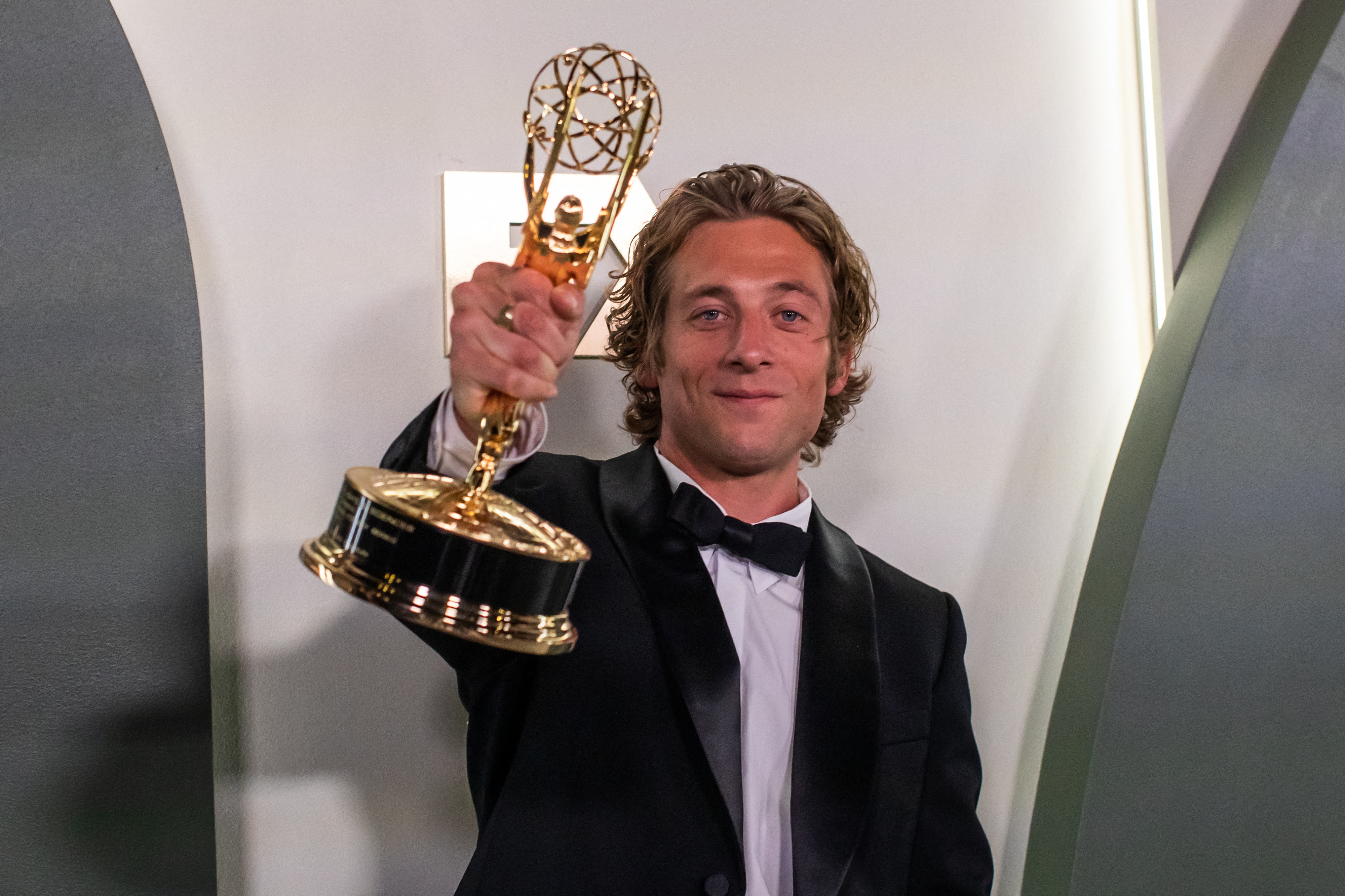 Jeremy Allen White holds up his Emmy trophy, smiling in a tuxedo with a bow tie