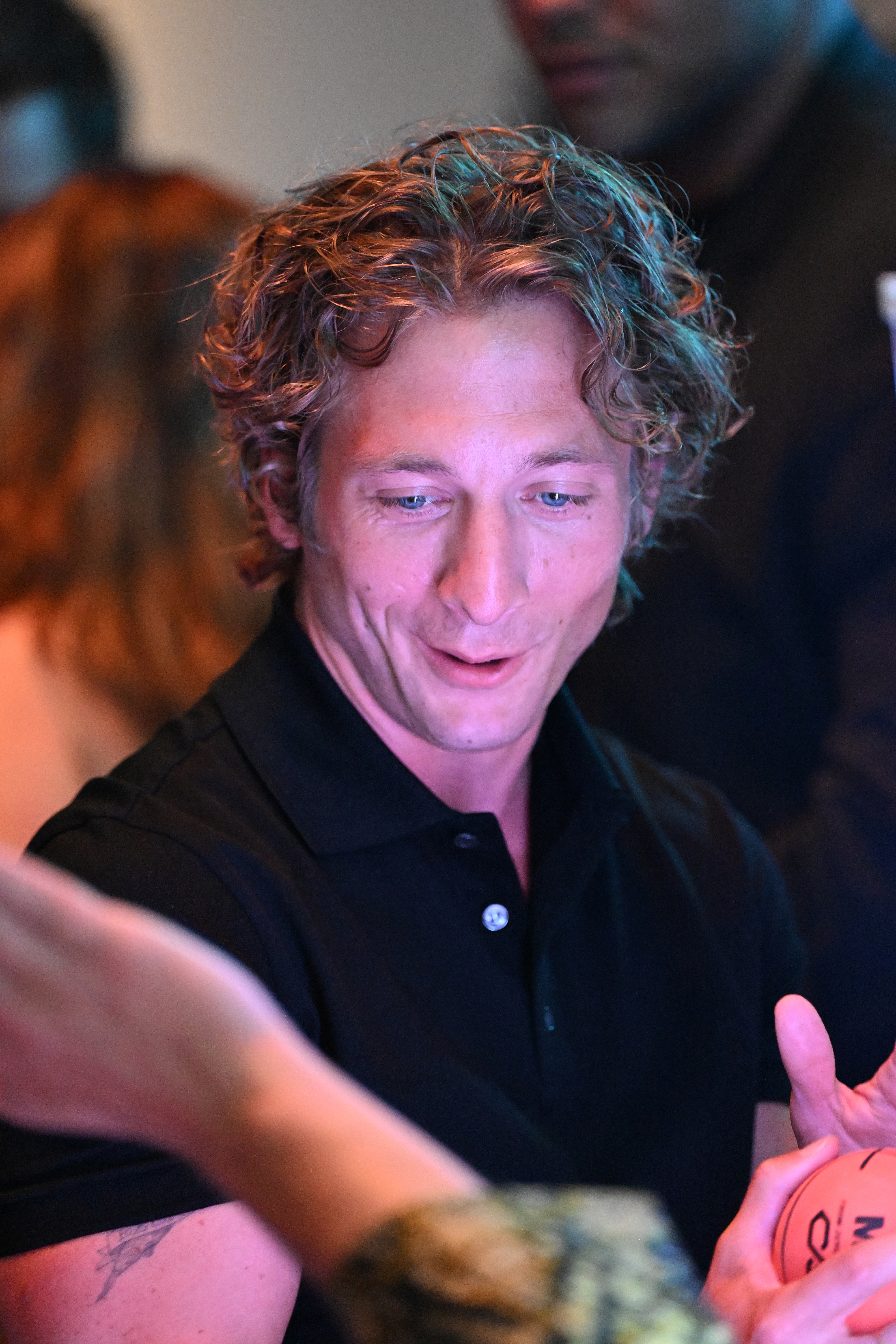 Jeremy Allen White is seen engaging in an animated conversation at a social event, wearing a polo shirt