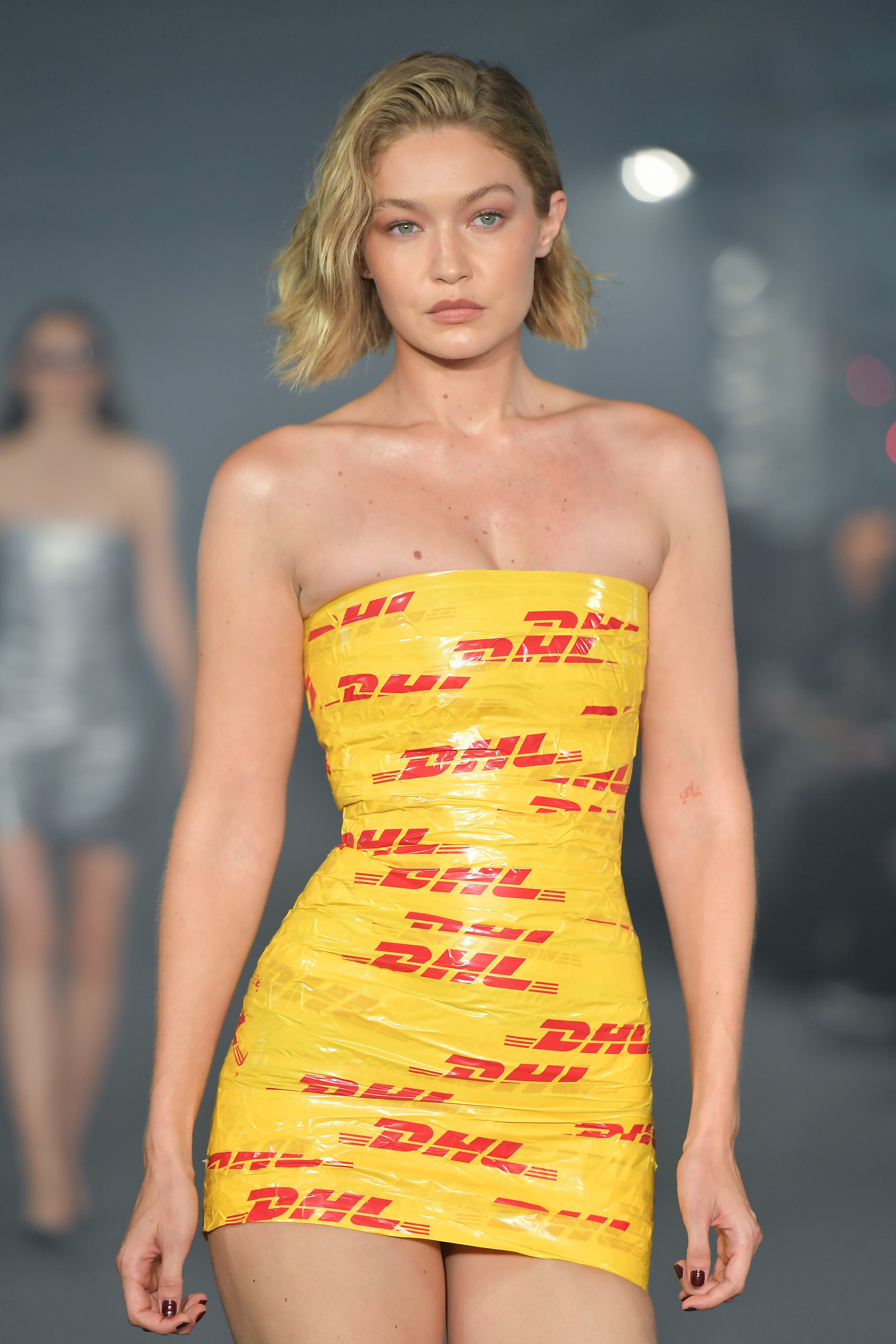 Gigi Hadid walks the runway in a strapless, body-hugging dress made of DHL-branded tape during a fashion show