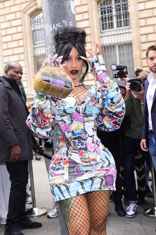 Cardi B in a graffiti-inspired dress, fishnet stockings, and a high updo, posing for photographers on a city street