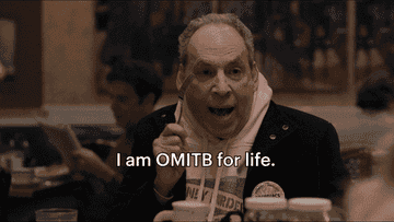 A character from &quot;Only Murders in the Building&quot; enthusiastically declares, &quot;I am OMITB for life,&quot; while sitting at a table inside a restaurant