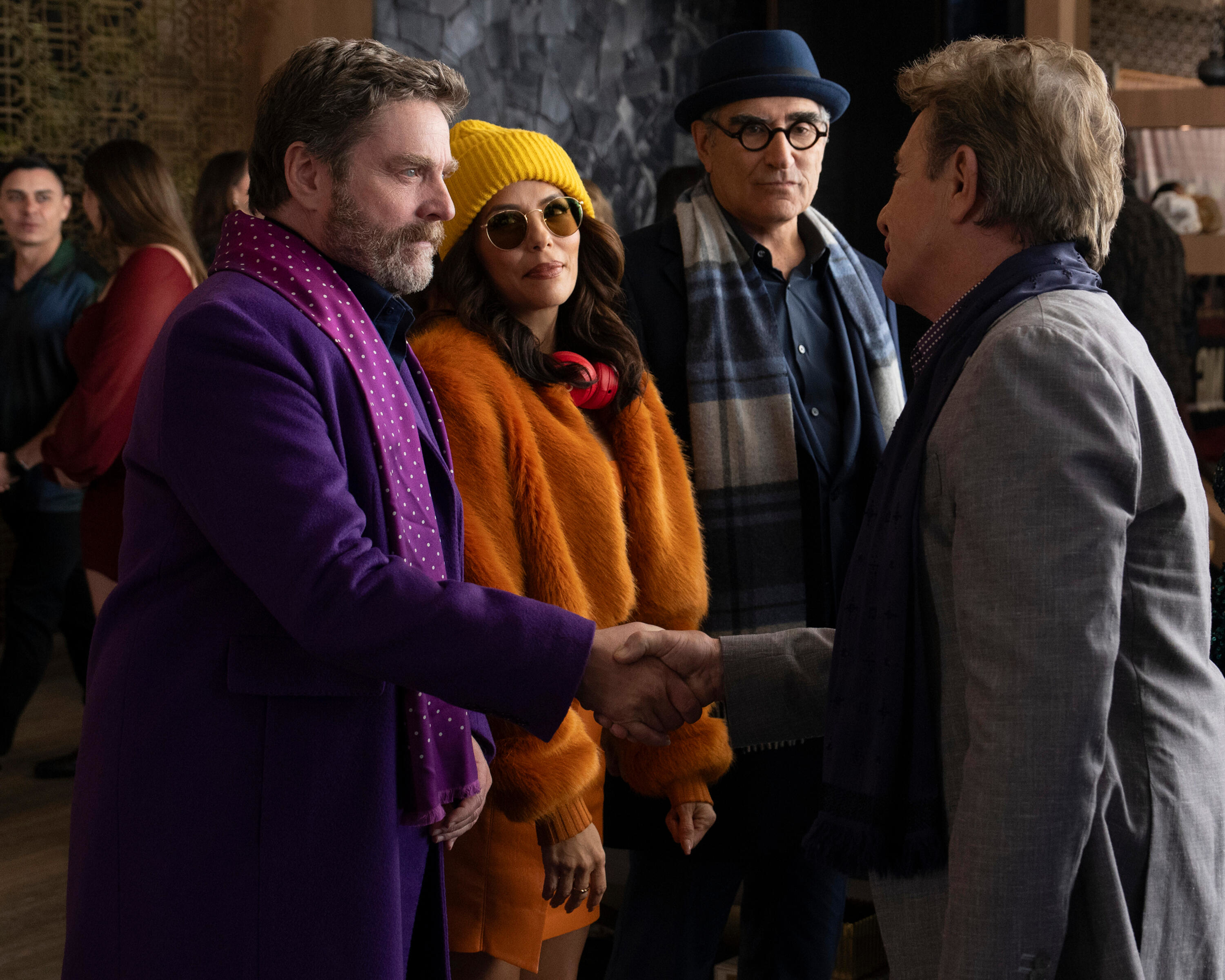 A person in a purple coat and a person in a gray coat shake hands, while two others in colorful outfits watch