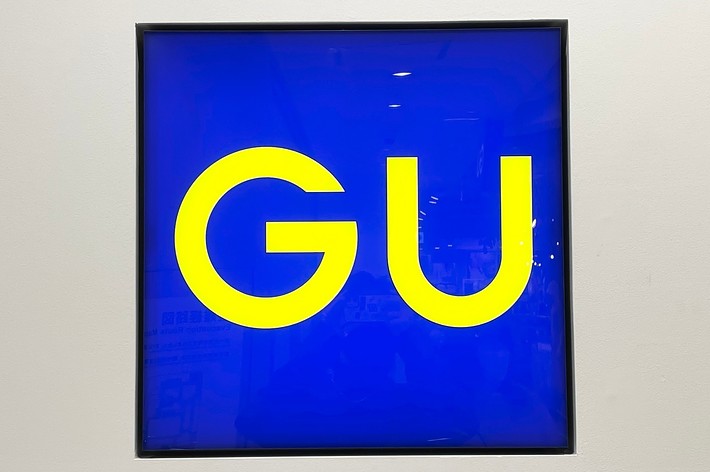 A square sign with a blue background and large yellow text that reads “GU."