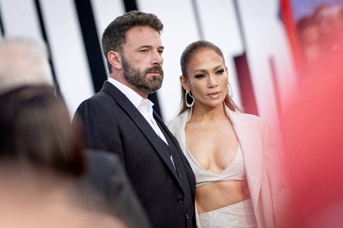 Ben Affleck and Jennifer Lopez on the red carpet. Ben is in a classic dark suit, while Jennifer is in an elegant, revealing outfit with large hoop earrings