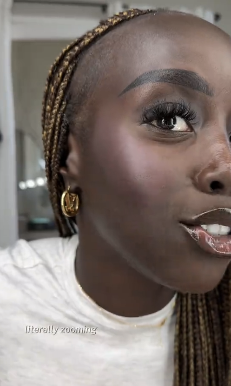 Close-up of Golloria giving a makeup tutorial on TikTok, wearing a white top and golden hoop earrings. TikTok sidebar and video titles are visible