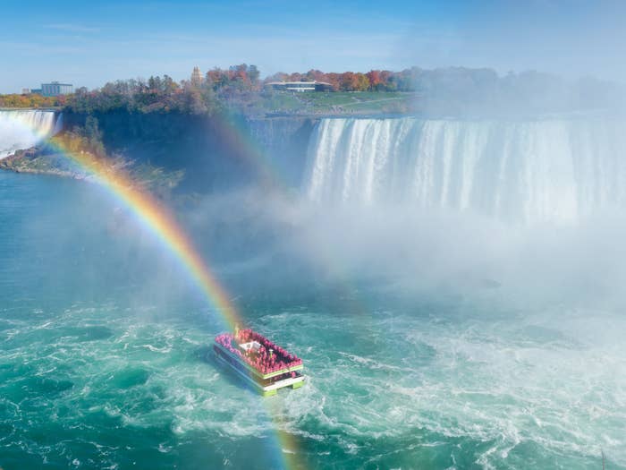 Boat with tourists approaches misty Niagara Falls with a vivid rainbow arching over the water