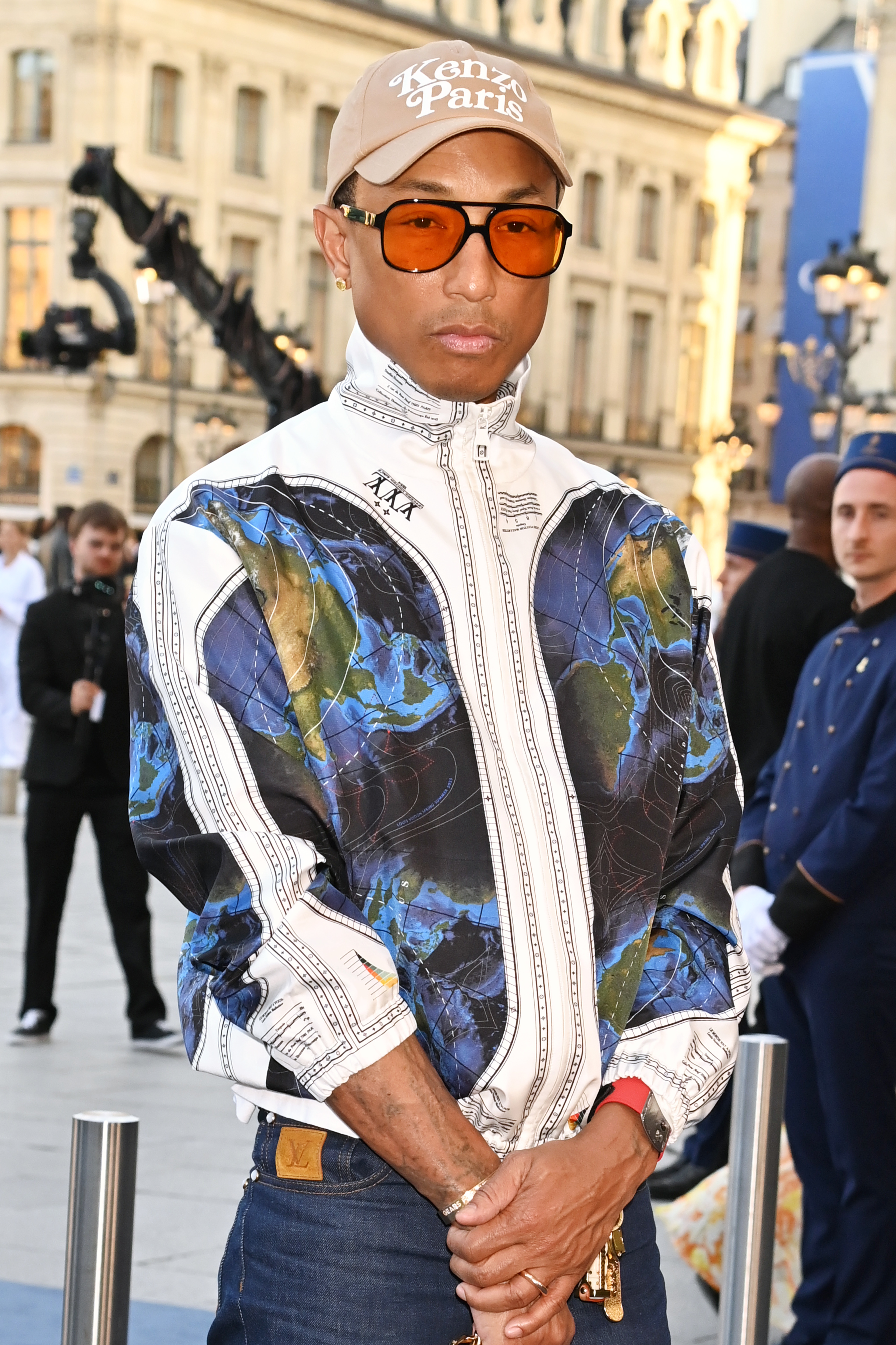 Pharrell Williams wearing an abstract print jacket and a 'Kenzo Paris' cap at an outdoor event