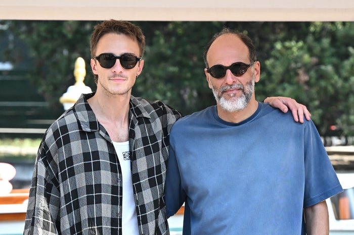 Drew Starkey and Luca Guadagnino, wearing casual attire and sunglasses, pose together outdoors with arms around each other