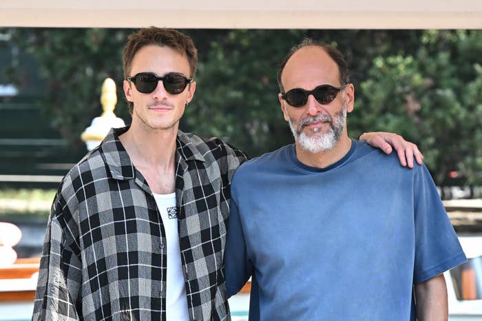 Drew Starkey and Luca Guadagnino, wearing casual attire and sunglasses, pose together outdoors with arms around each other