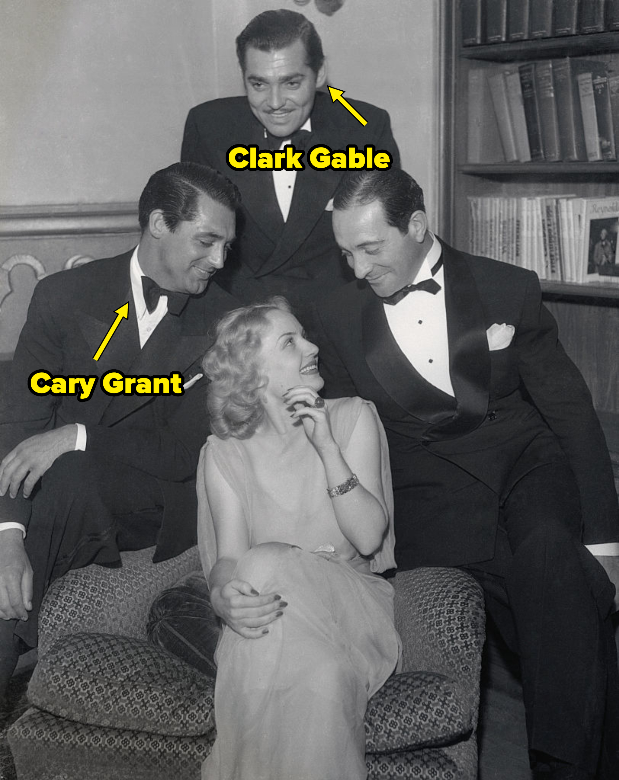 Carole Lombard sits on a couch smiling at Cary Grant, Clark Gable, and Jack Oakie, who are all wearing tuxedos