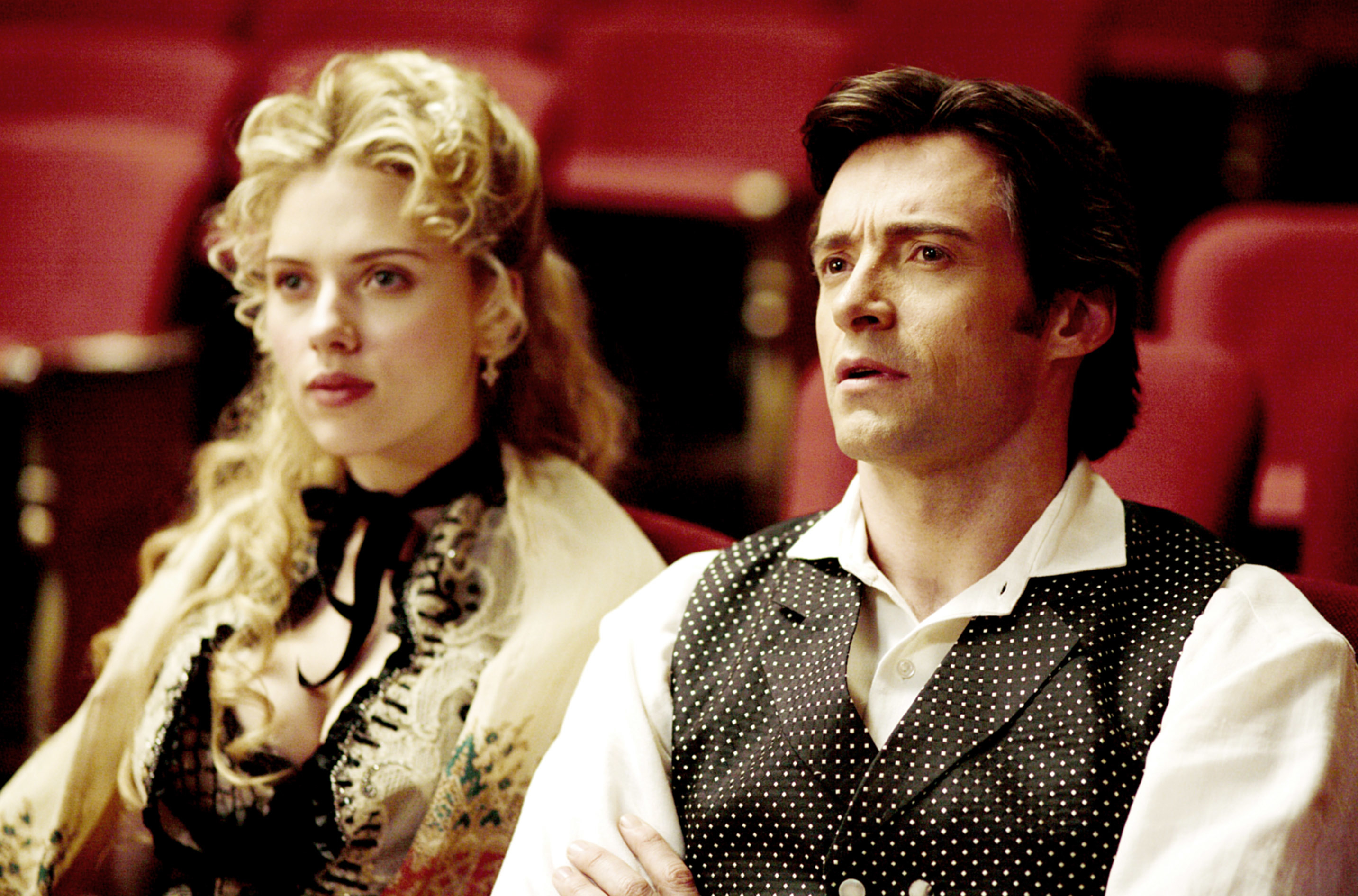 Scarlett Johansson and Hugh Jackman in period costumes sitting in a theater scene from a movie
