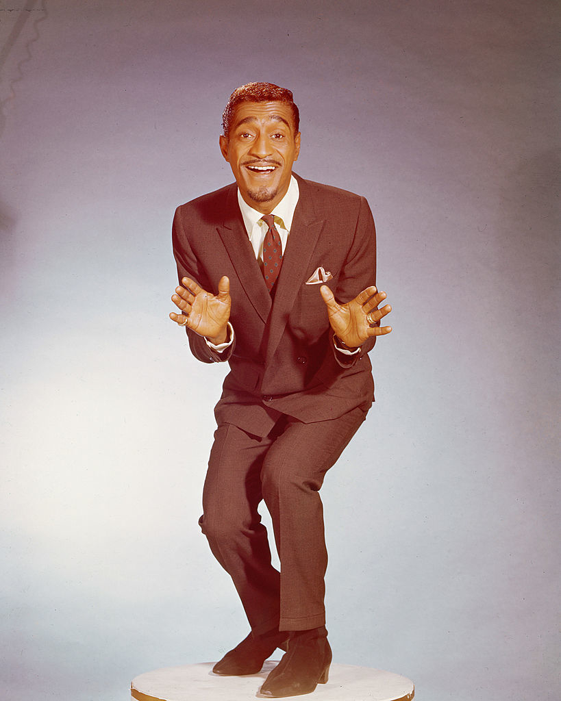 Sammy Davis Jr. joyfully poses mid-dance in a tailored suit and tie, exuding charm and energy