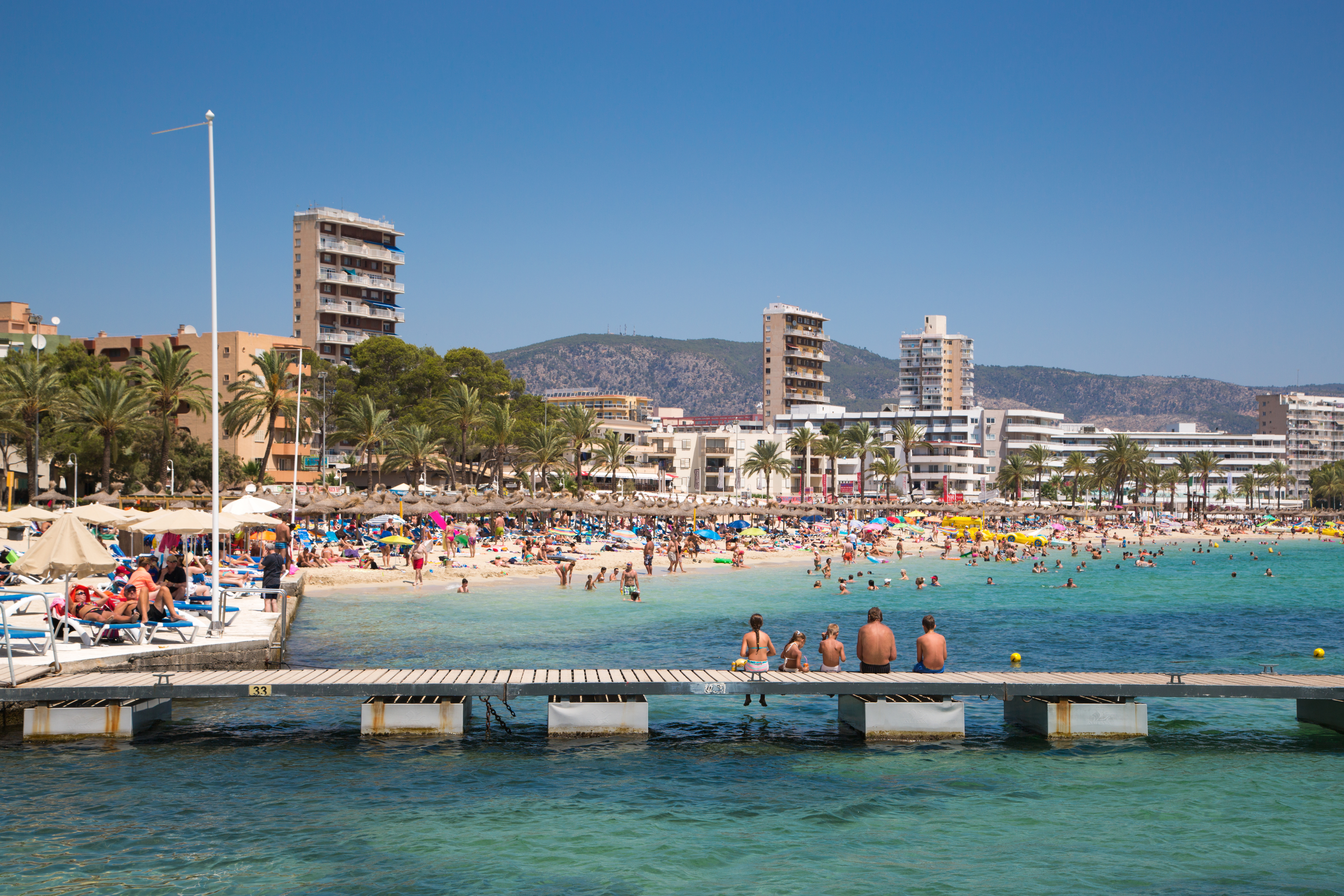 A crowded beach in Magaluf, Majorca with people sunbathing, swimming, and walking