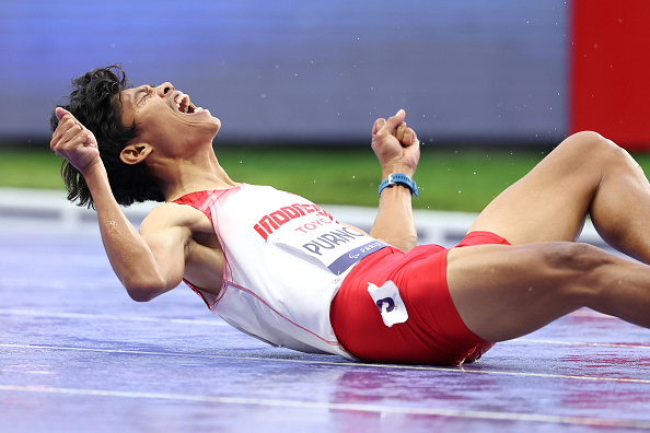 Olympic athlete at Tokyo 2020 celebrating on the track after winning a race, wearing a white and red uniform with "PUKHTO" visible on the front