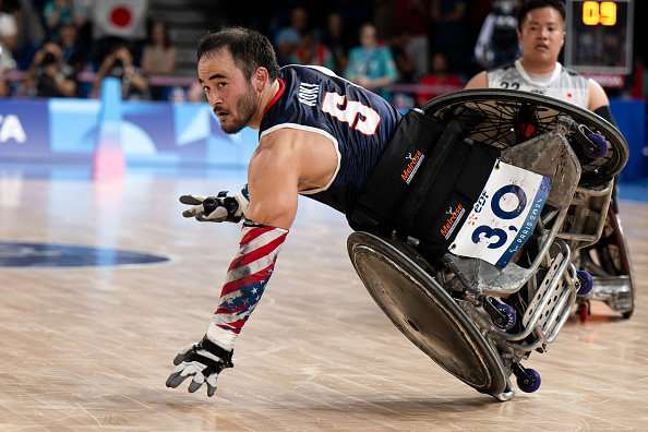 Paralympian Chuck Aoki in a wheelchair on the court during a rugby match, wearing a jersey with No. 3, alongside another athlete in the background