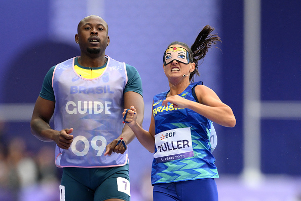 Brazilian paralympian Thalita Simplicio running with her guide at the World Para Athletics Championships, with Muller bib and superhero face paint