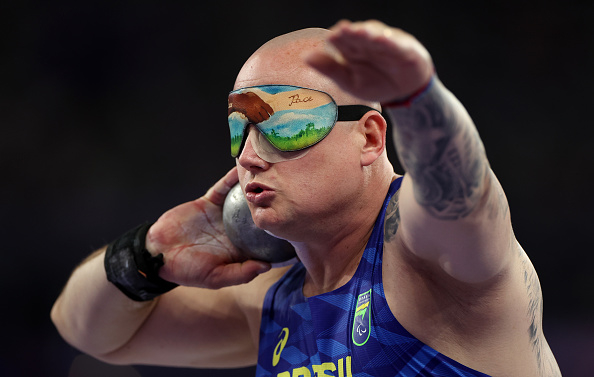Paralympic athlete Thiago Paulino, wearing a blindfold, prepares to throw a shot put at a sports event