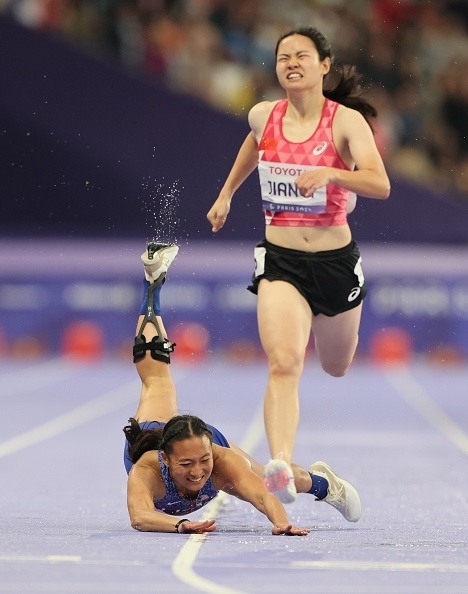 Track event: A runner falls while another runner, Jiang Fenfen, sprints past her. The fallen runner’s athletic prosthetic leg is visible in the image