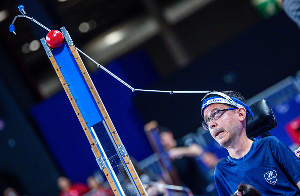 A person in a wheelchair competes in a Boccia game, focused on aiming the ball with the help of an assistive device