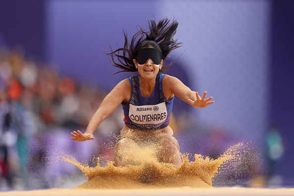 Paralympian Monica Olivia Rodriguez Colmenares lands in the sand during a long jump event at a track and field competition, wearing a blindfold and sports attire